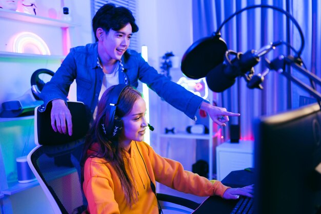 Caucasian woman gamer and Asian male coach celebrating victory together in front of the gaming table